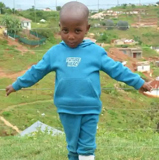 A little boy standing with his arms out wide. Behind him is the Valley of a 1000 Hills. Project Hope ECD