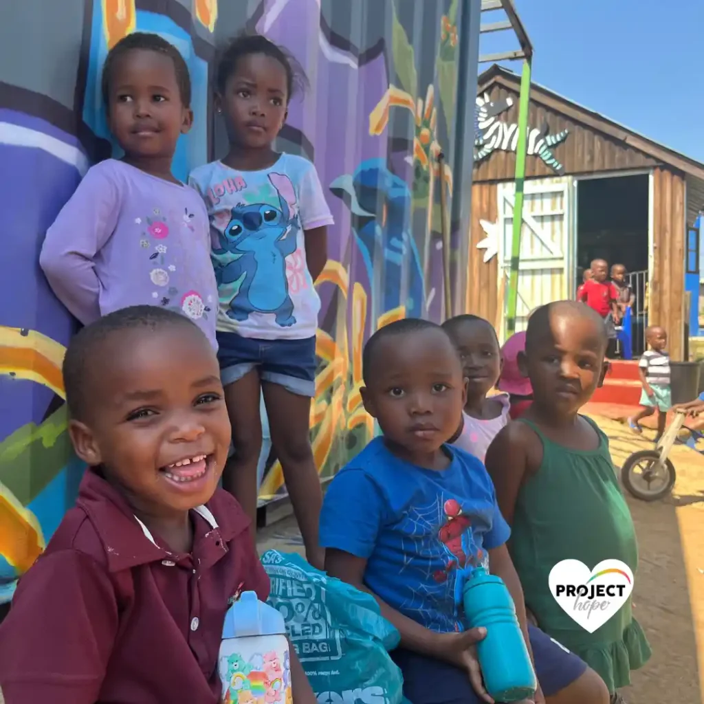 Toddlers smiling and playing during a tea break. Project Hope provides safe spaces, ECD preschool, South Africa.