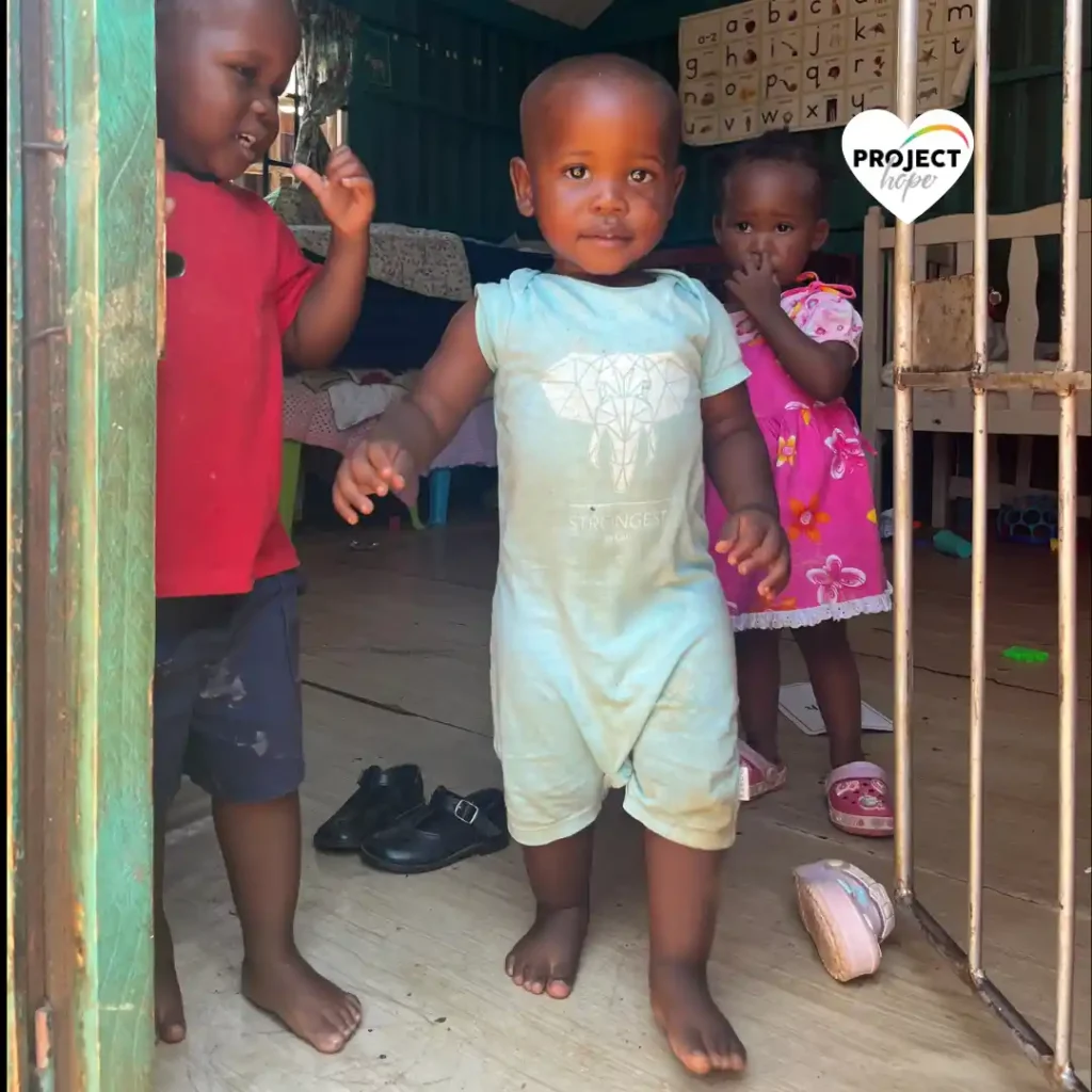Three young children stand curiously in the doorway of a Project Hope learning centre in the Valley of 1000 Hills.