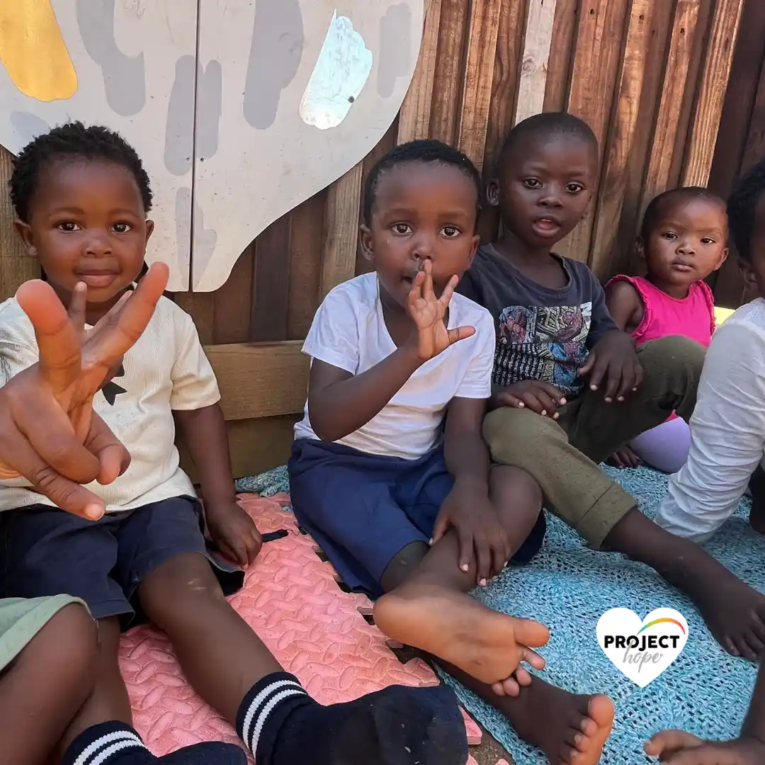 Young children in the Project Hope program (Early Childhood Development in South Africa) sit together and smile for a photo.