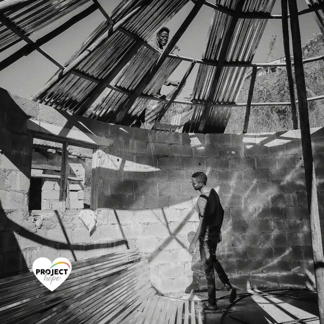 Black and white photograph showing the construction of the Embo Skills Hut with workers securing a traditional rondavel-style roof structure. This is how Section 18A ECD Donations make a positive impact to vulnerable communities.