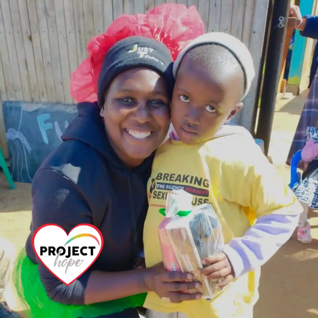 support-an-ecd-centre-nonto-manager A smiling community early childhood development teacher (Nonto) hugs a young preschool student outside a local centre.